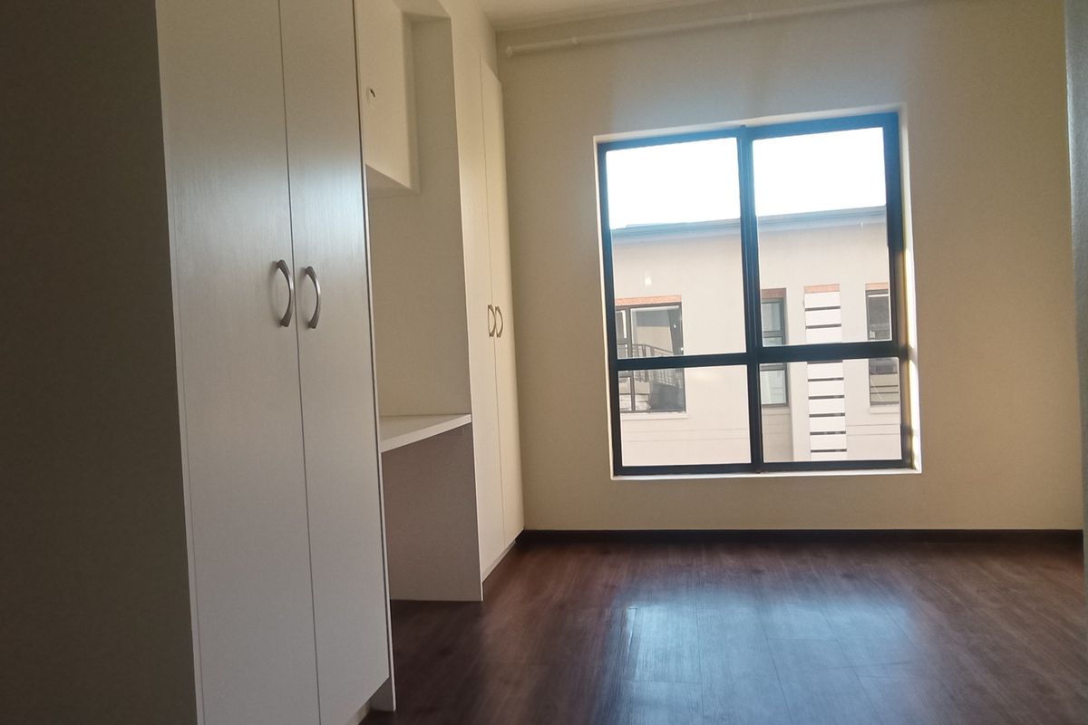 A bright, empty bedroom featuring modern laminate flooring, built-in cupboards, and a convenient integrated desk space.
