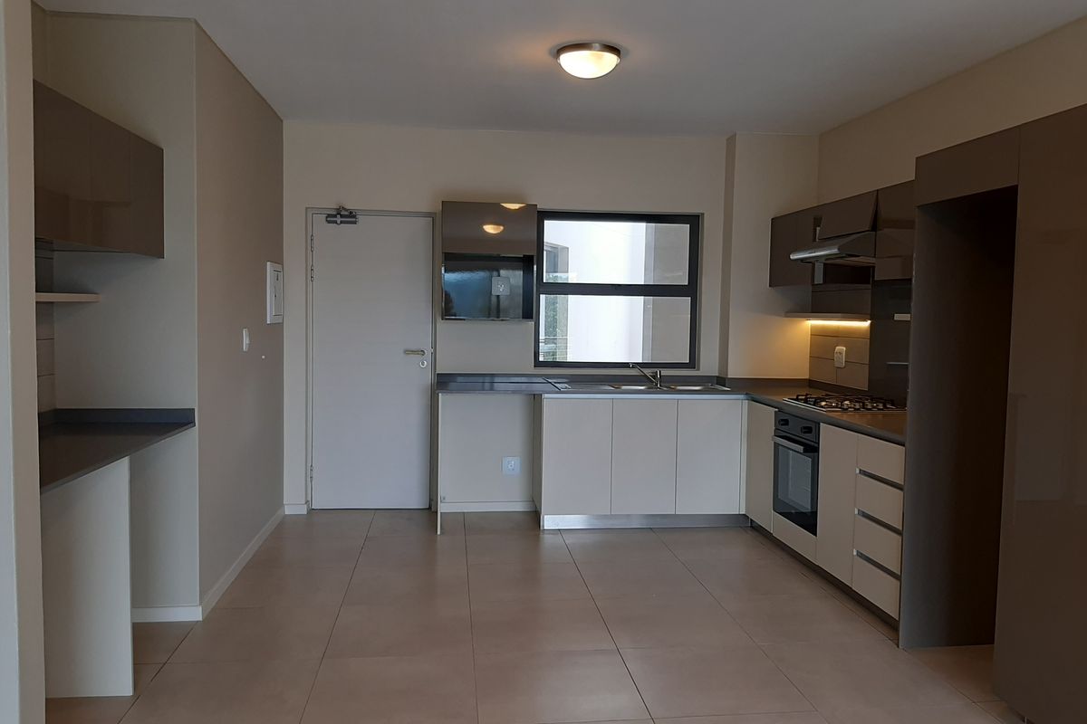 Modern open-plan kitchen featuring sleek cabinetry, built-in oven, gas hob, extractor fan, and tiled flooring in a contemporary apartment setting.