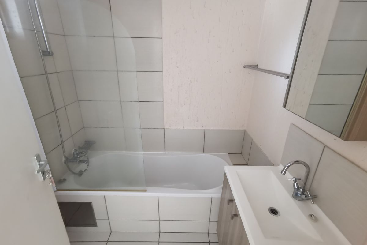A functional bathroom featuring a bathtub with a glass shower screen, a vanity basin, and neutral wall and floor tiling.