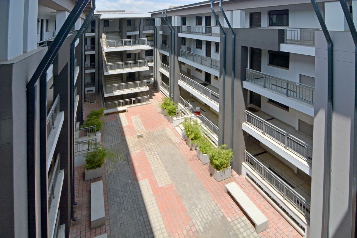 An elevated view of a modern apartment complex courtyard featuring paved walkways, metal balcony railings, and communal stairwell access.
