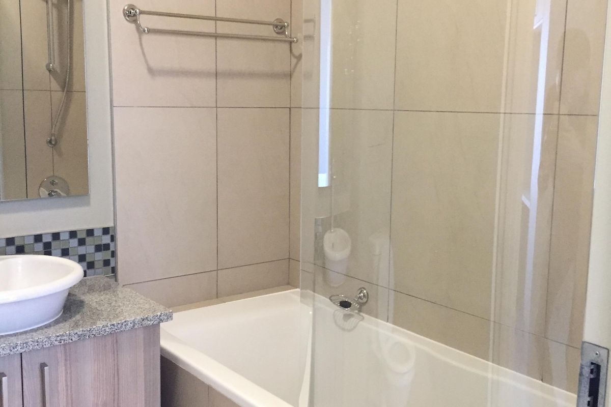 A clean, modern bathroom featuring a vanity with granite countertop, vessel sink, and a bathtub with a glass shower screen and wall tiling.