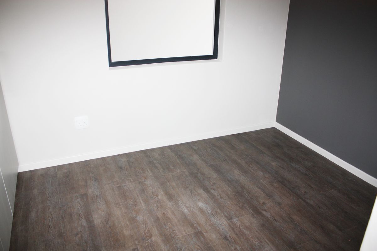 An empty bedroom featuring modern dark laminate flooring and a contrasting grey accent wall.