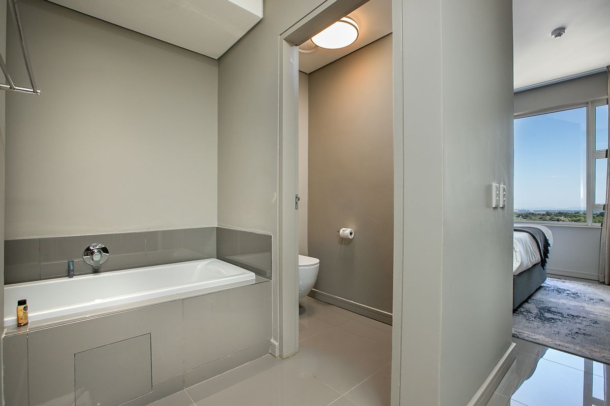 Modern bathroom featuring a built-in bathtub with tiled surround, adjacent to a private toilet enclosure, with neutral finishes and clean lines.