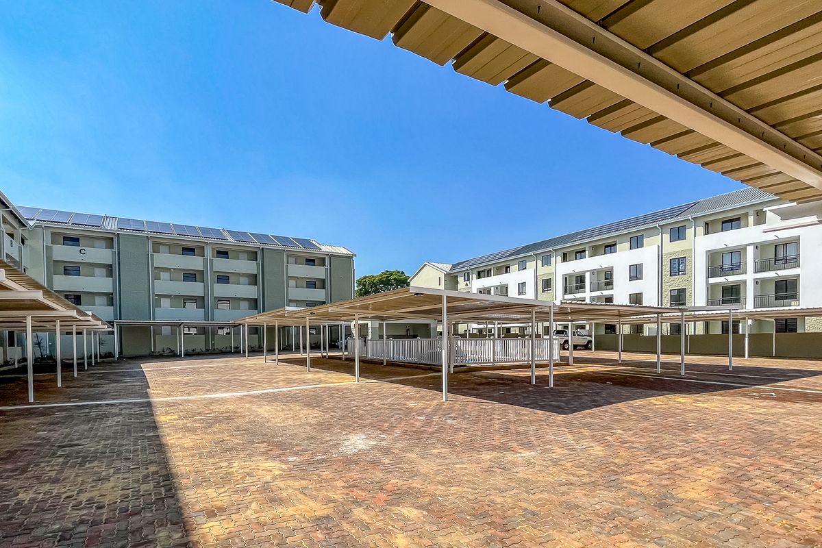 A view of the apartment complex parking area featuring covered parking bays and paved ground surfaces.