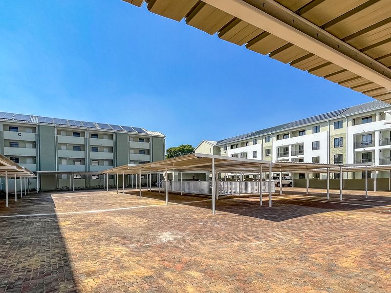 A view of the apartment complex parking area featuring covered parking bays and paved ground surfaces.