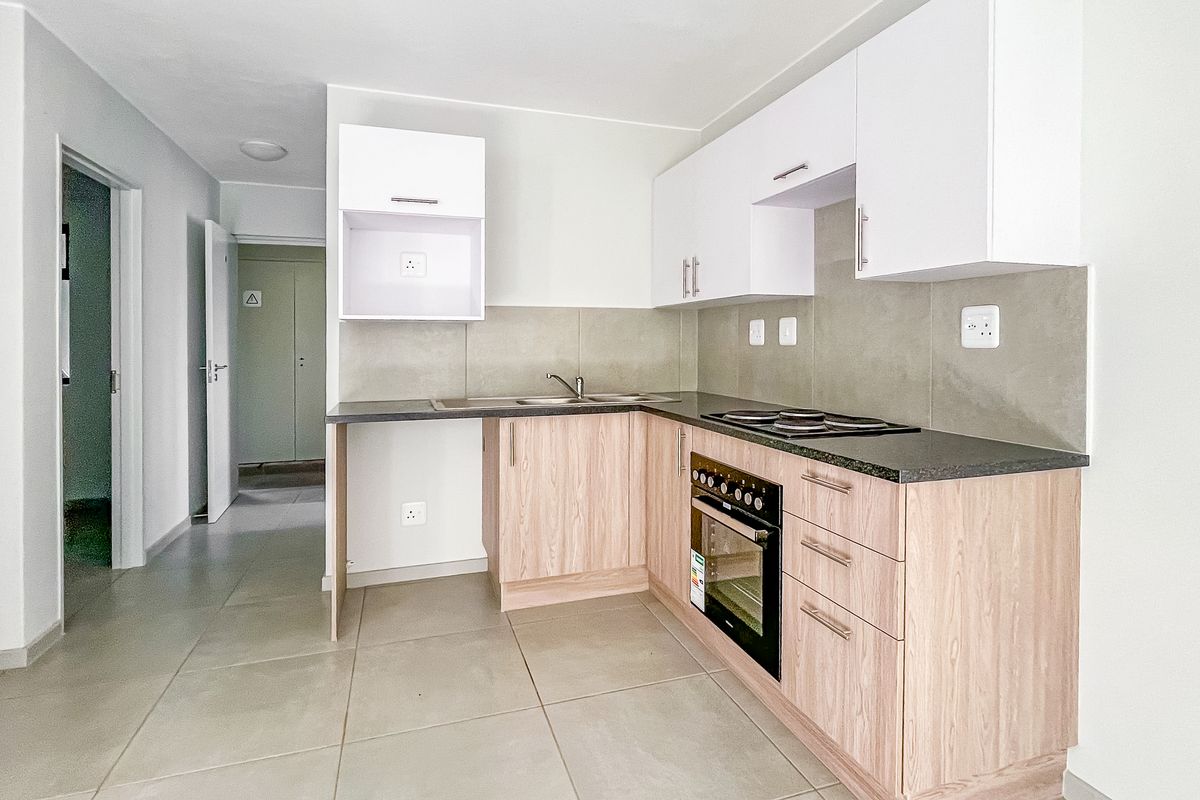 Modern kitchen featuring light wood cabinetry, dark countertops, built-in oven, electric hob, and tiled flooring in an open-plan layout.