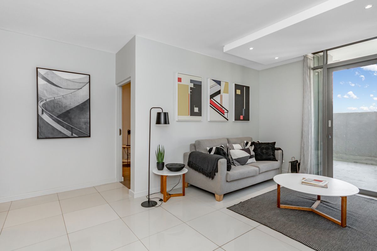 Modern living room featuring sleek tiled flooring, recessed ceiling lighting, and a large sliding glass door providing access to the balcony.