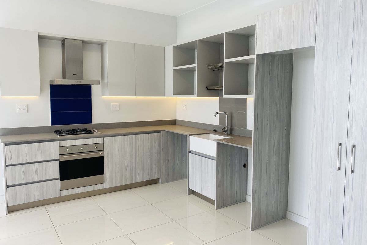 Modern kitchen featuring light wood-grain cabinetry, a farmhouse sink, built-in oven, gas hob, and sleek tiled flooring in a clean, contemporary space.