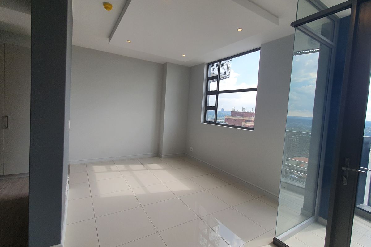 A bright, modern, and empty bedroom featuring large windows with expansive city views, tiled flooring, and recessed ceiling lighting.
