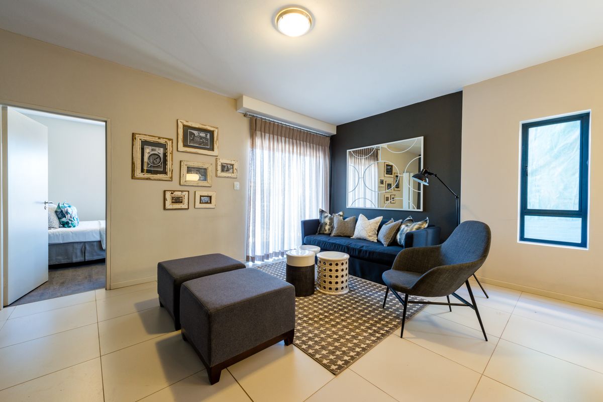 A well-lit living room featuring neutral tiled flooring, a dark accent wall, and a sliding glass door providing access to the exterior.