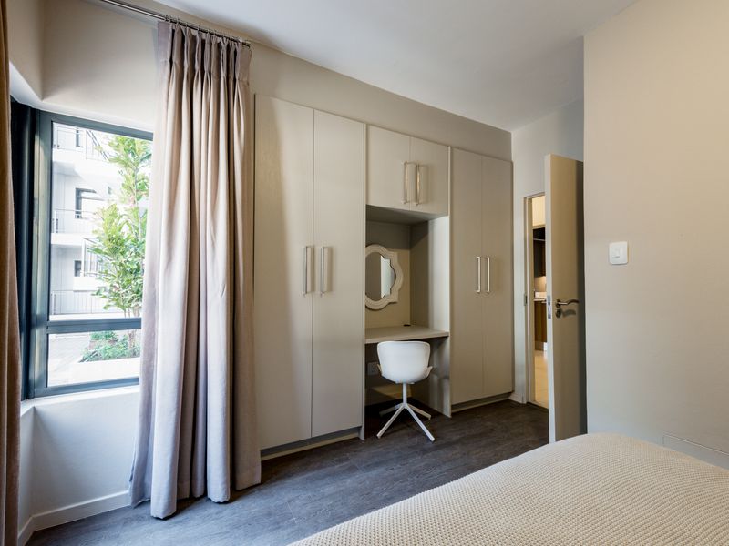 A well-maintained bedroom featuring modern built-in cupboards with an integrated vanity station and durable laminate flooring.