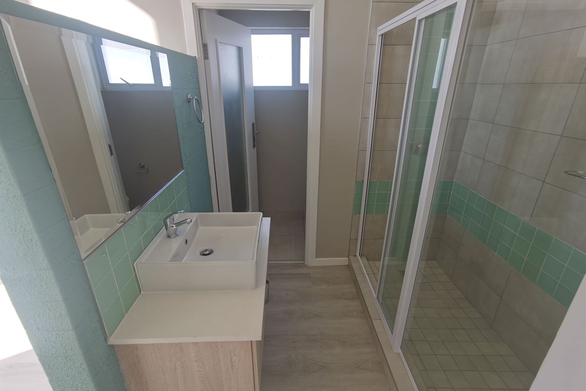 Modern bathroom featuring a floating vanity with vessel sink, large wall mirror, and a glass-enclosed shower with decorative tiled accents.