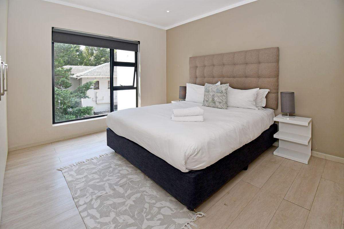 A well-maintained bedroom featuring light wood-look flooring, neutral wall tones, and a large window providing natural light and a view of the surroundings.