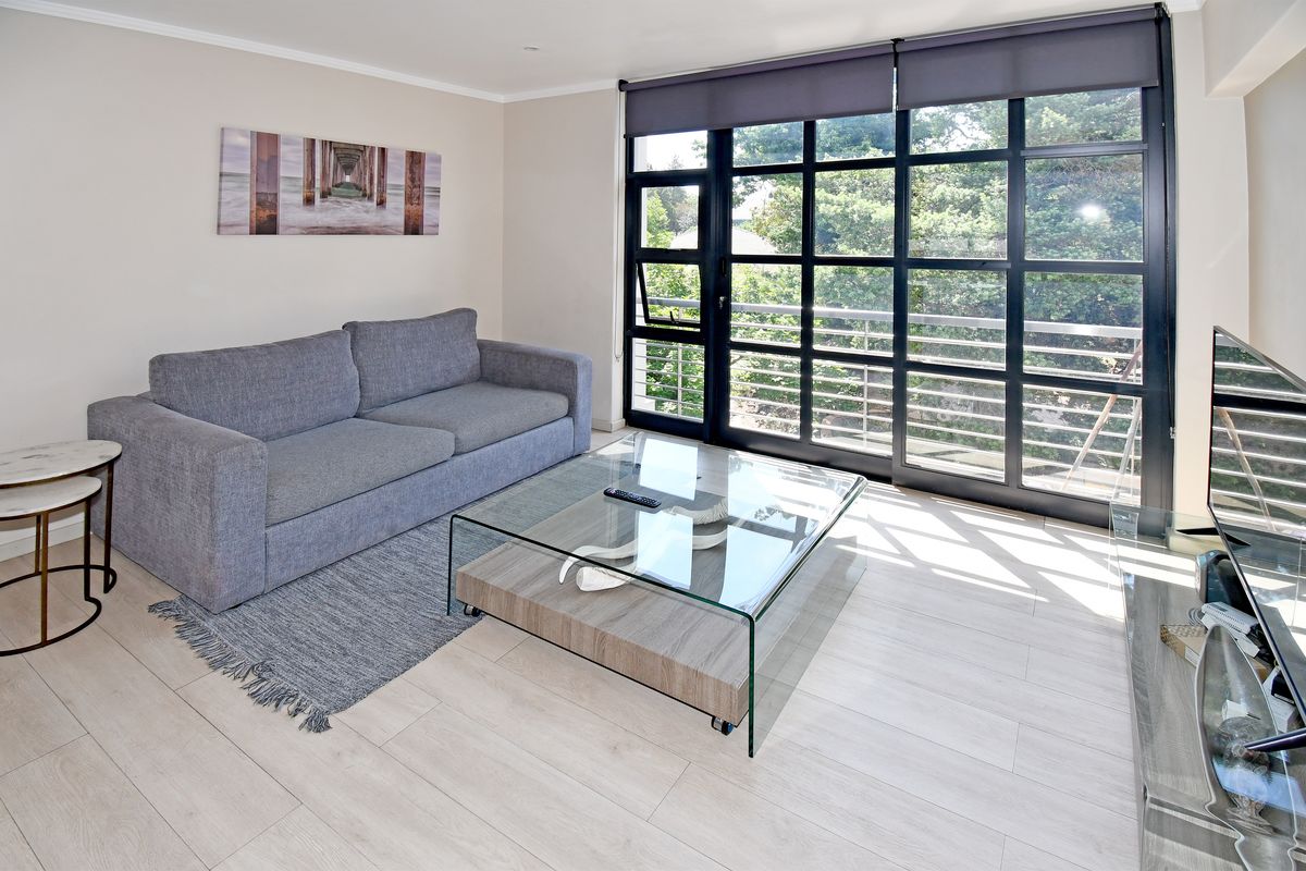 Bright and modern living room featuring large black-framed glass sliding doors that open onto a balcony, providing ample natural light and scenic views.