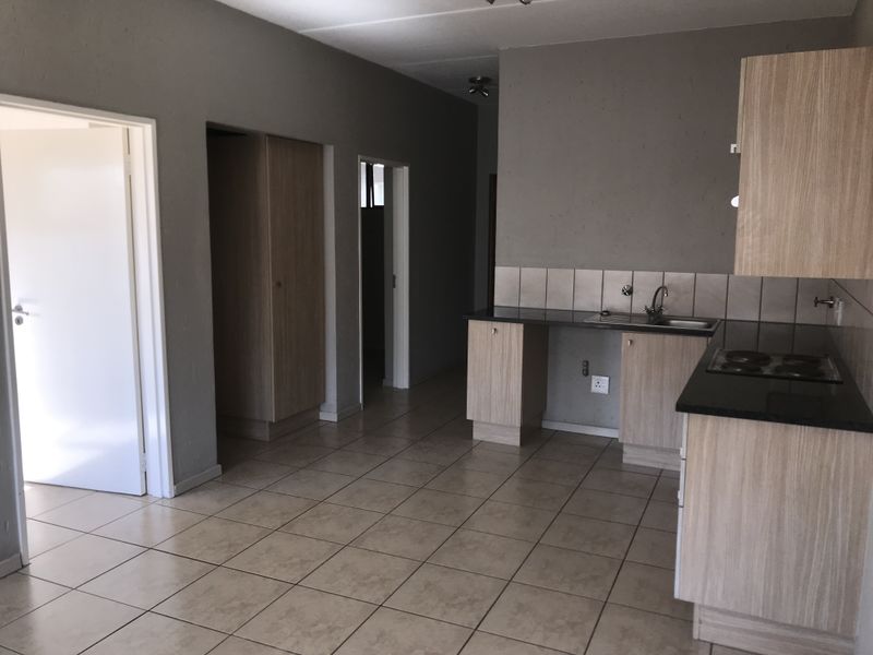 Open-plan kitchen area featuring built-in cabinetry, dark laminate countertops, an electric hob, and tiled flooring throughout the living space.