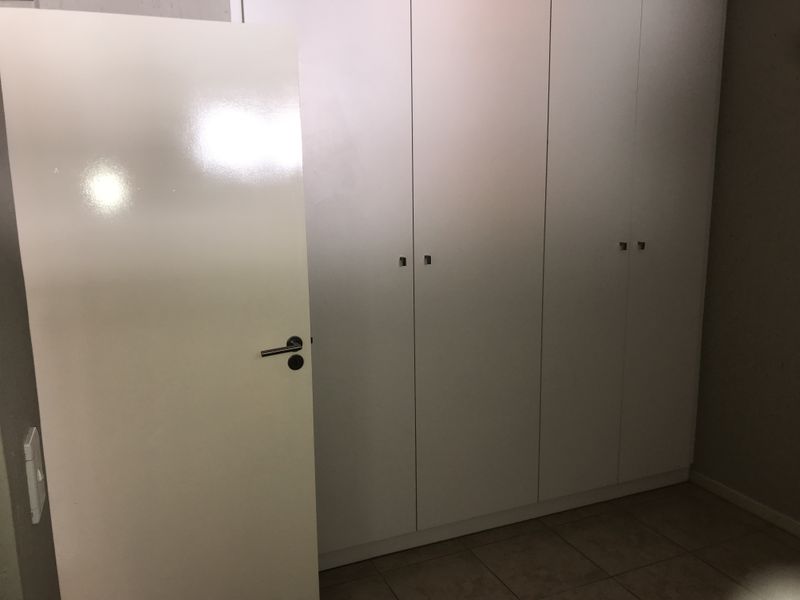 A bedroom interior featuring built-in white cupboards and tiled flooring, presented in a clean, vacant state.