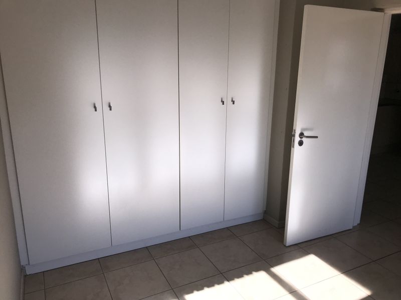A clean, empty bedroom featuring neutral tiled flooring and ample built-in cupboard storage space.
