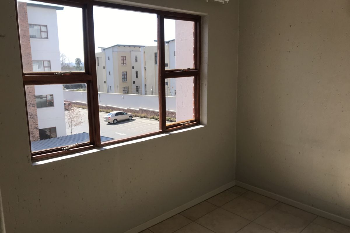 An empty bedroom featuring tiled flooring and timber-framed windows with views of the surrounding apartment complex.