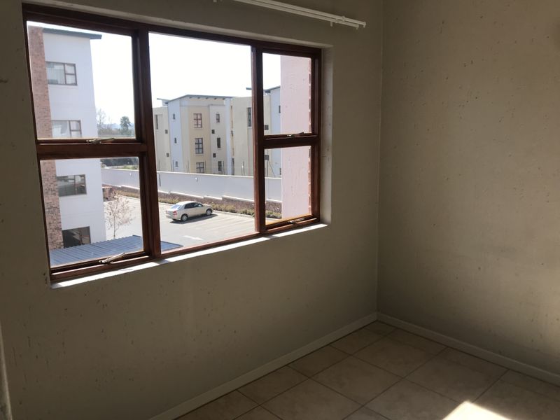 An empty bedroom featuring tiled flooring and timber-framed windows with views of the surrounding apartment complex.