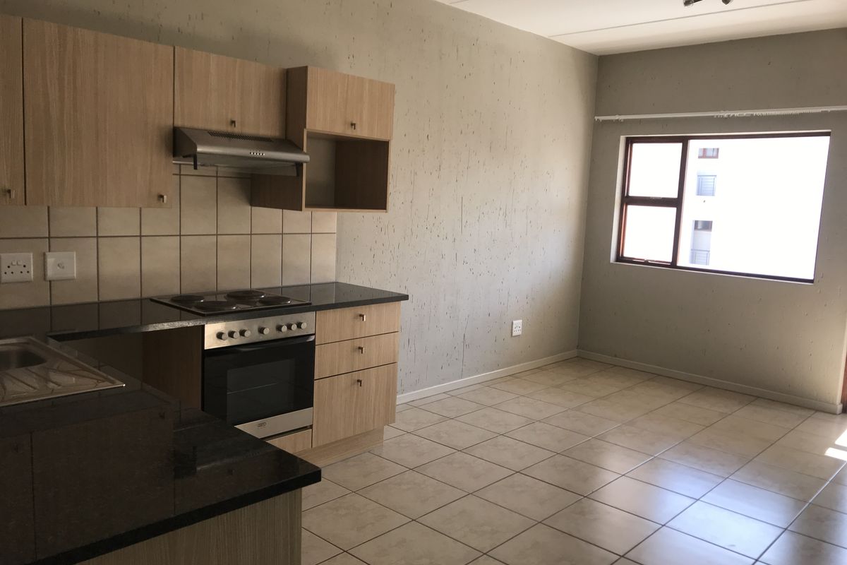 Open-plan kitchen and living area featuring light wood cabinetry, granite countertops, built-in oven, and tiled flooring throughout.