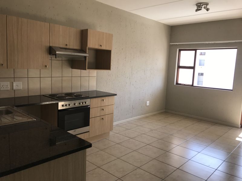 Open-plan kitchen and living area featuring light wood cabinetry, granite countertops, built-in oven, and tiled flooring throughout.
