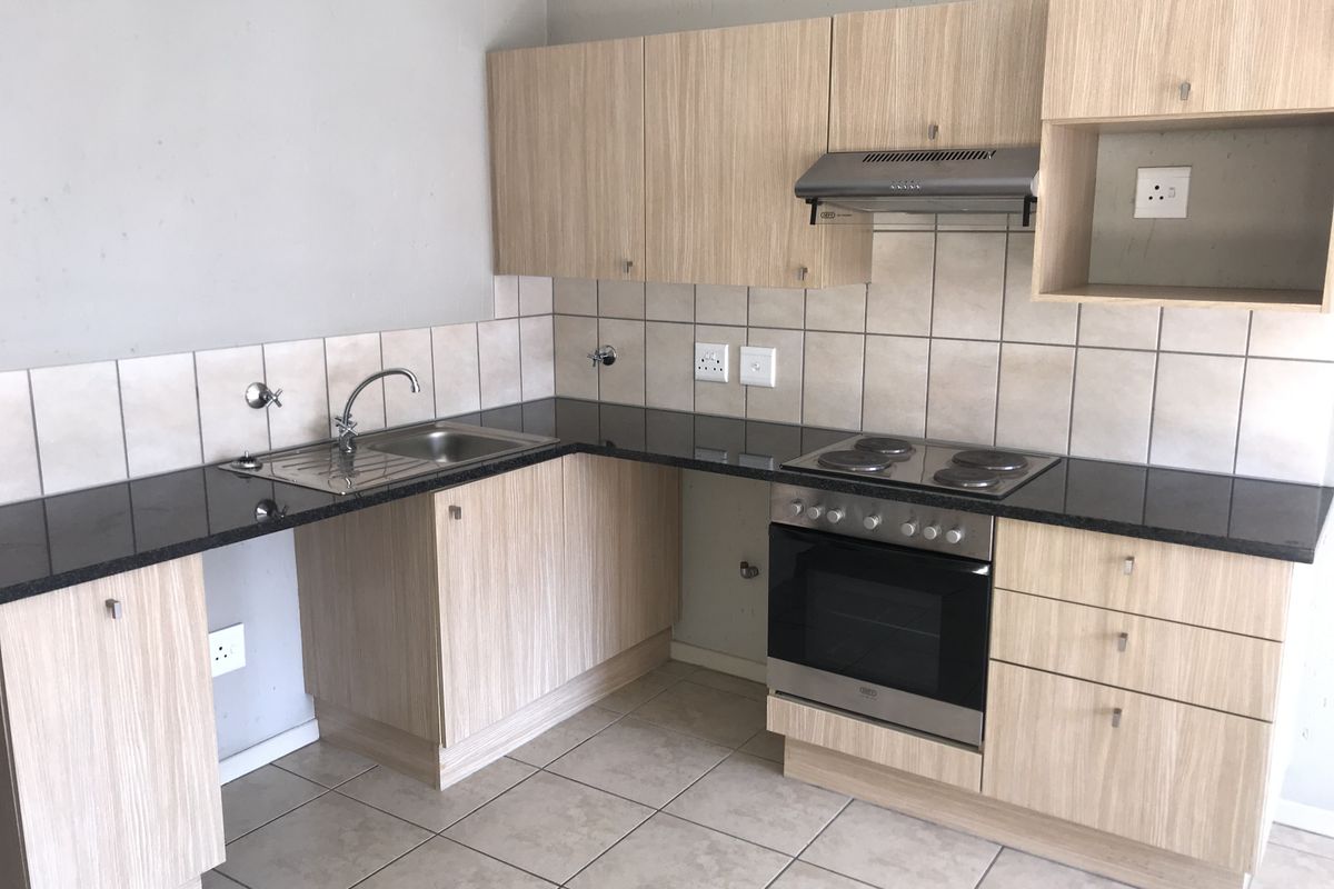 A functional kitchen featuring light wood-finish cabinetry, granite countertops, built-in oven, electric hob, and extractor fan, with tiled splashbacks and flooring.