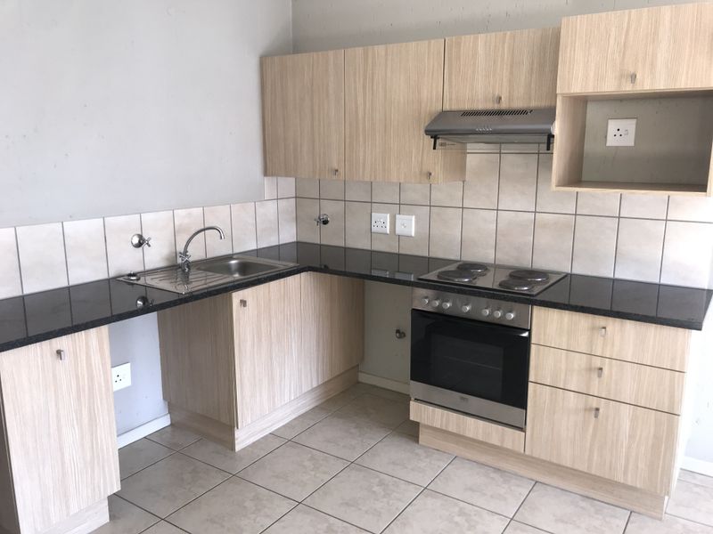 A functional kitchen featuring light wood-finish cabinetry, granite countertops, built-in oven, electric hob, and extractor fan, with tiled splashbacks and flooring.