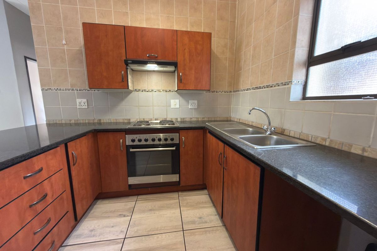 A functional kitchen featuring wood-finish cabinetry, granite countertops, a built-in oven with hob, and a double stainless steel sink with tiled splashbacks.