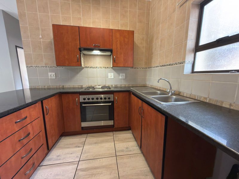 A functional kitchen featuring wood-finish cabinetry, granite countertops, a built-in oven with hob, and a double stainless steel sink with tiled splashbacks.