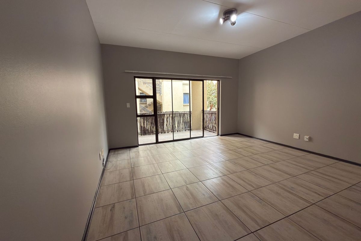 A spacious, empty living room featuring neutral grey walls, modern wood-look tiled flooring, and a large sliding glass door leading to a balcony.