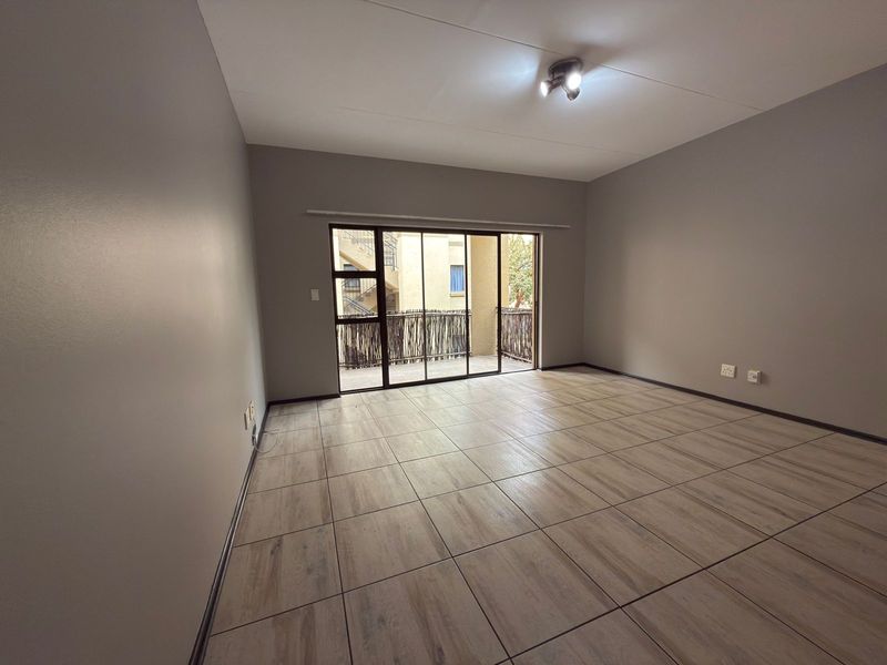 A spacious, empty living room featuring neutral grey walls, modern wood-look tiled flooring, and a large sliding glass door leading to a balcony.