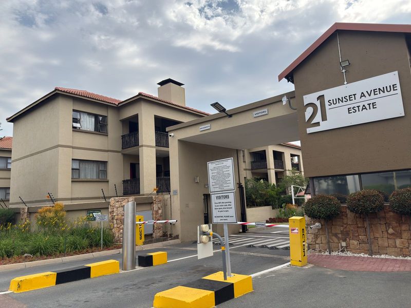 The entrance to 21 Sunset Avenue Estate, featuring a secure boom gate access point, stone-clad pillars, and well-maintained apartment building architecture.