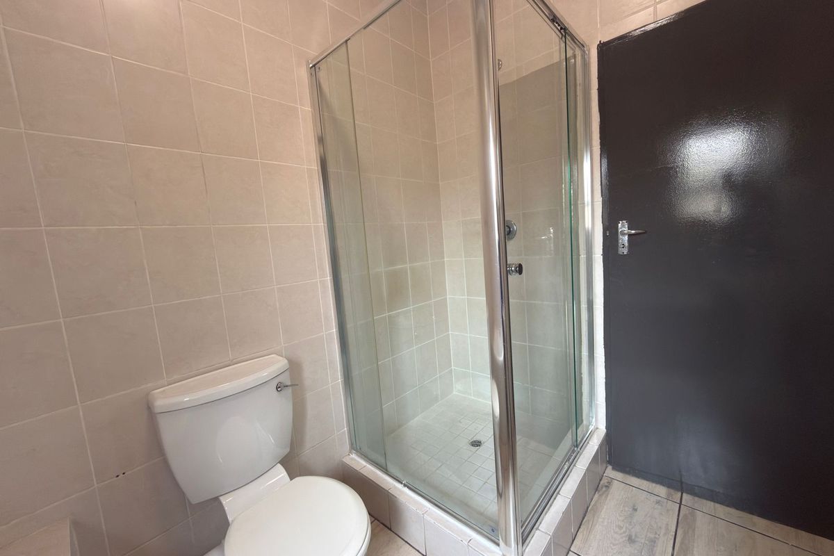 A functional bathroom featuring a corner shower enclosure, a standard toilet, and neutral wall and floor tiling.