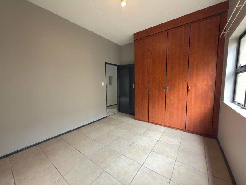 A clean, empty bedroom featuring tiled flooring and a large, built-in wooden wardrobe providing ample storage space.