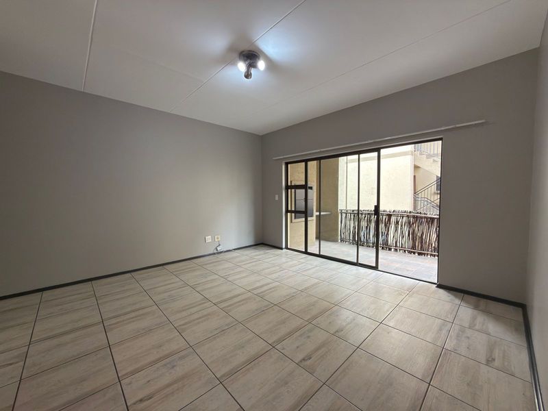 An empty, well-maintained living room featuring neutral tiled flooring and a large sliding glass door providing access to an outdoor balcony area.
