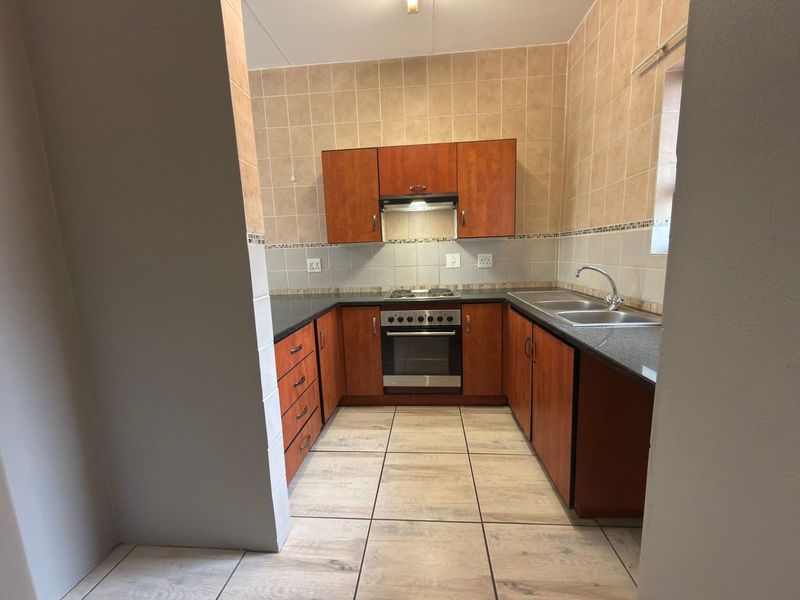 A functional kitchen featuring wooden cabinetry, granite countertops, a built-in oven with hob, and tiled finishes throughout.