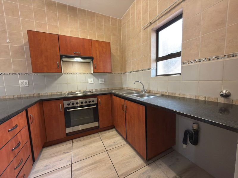 A functional kitchen featuring wood-finish cabinetry, granite countertops, a built-in oven with hob, and tiled finishes throughout.