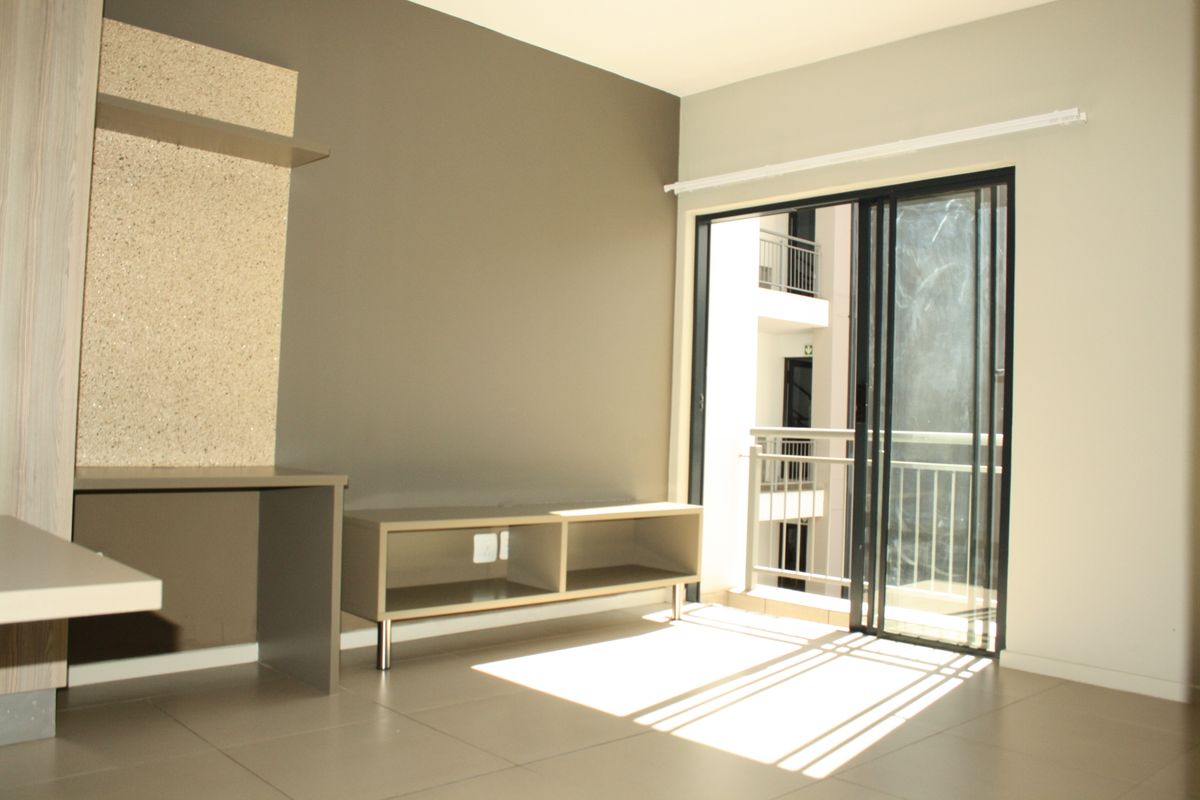 A bright living area featuring built-in cabinetry, tiled flooring, and sliding glass doors that open onto a balcony.