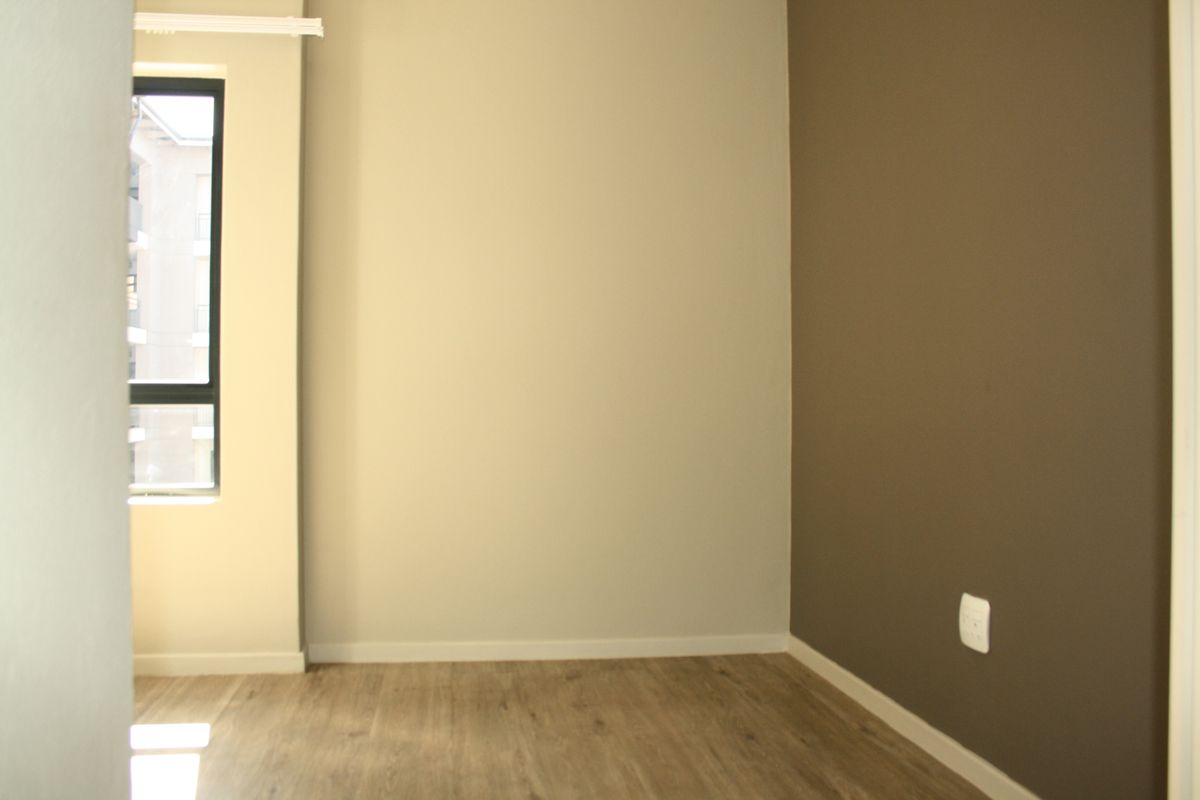 A bright, empty bedroom featuring modern wood-look laminate flooring and a contrasting accent wall.