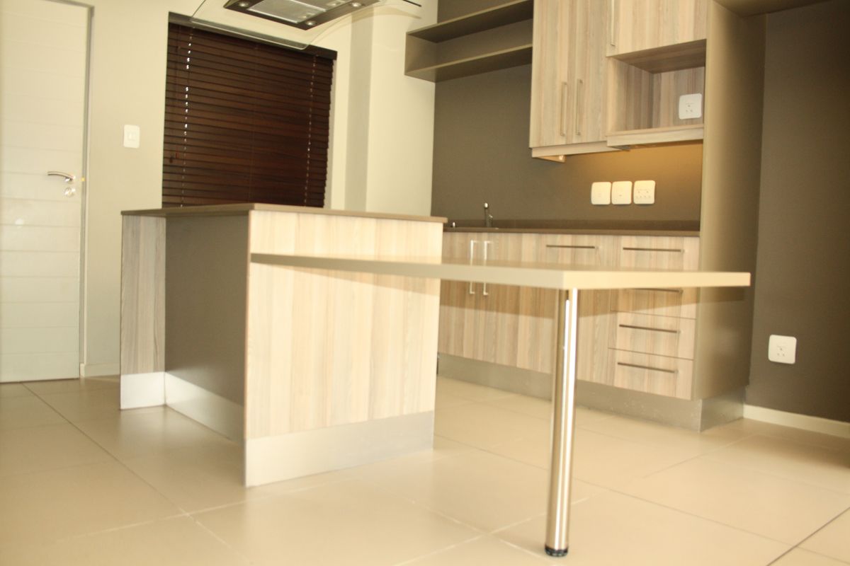 Modern kitchen featuring light wood-grain cabinetry, a central island with an integrated breakfast bar, and sleek tiled flooring.