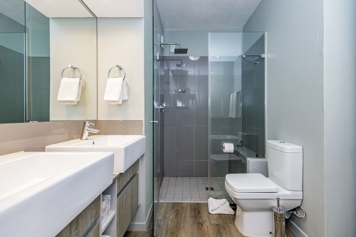 Modern bathroom featuring a double vanity with integrated sinks, a glass-enclosed walk-in shower with tiled walls, and a contemporary toilet.