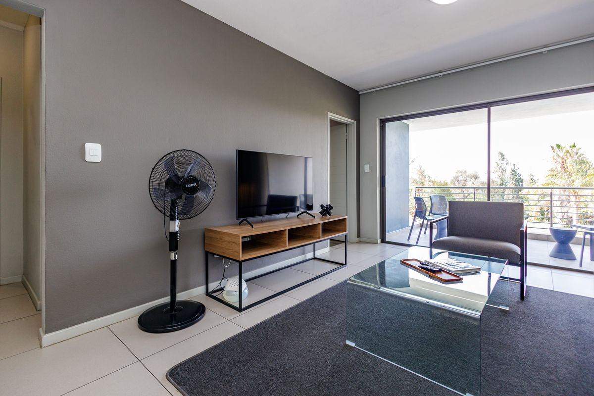 A modern living room featuring neutral grey walls, large format floor tiles, and sliding glass doors that open onto a private balcony.