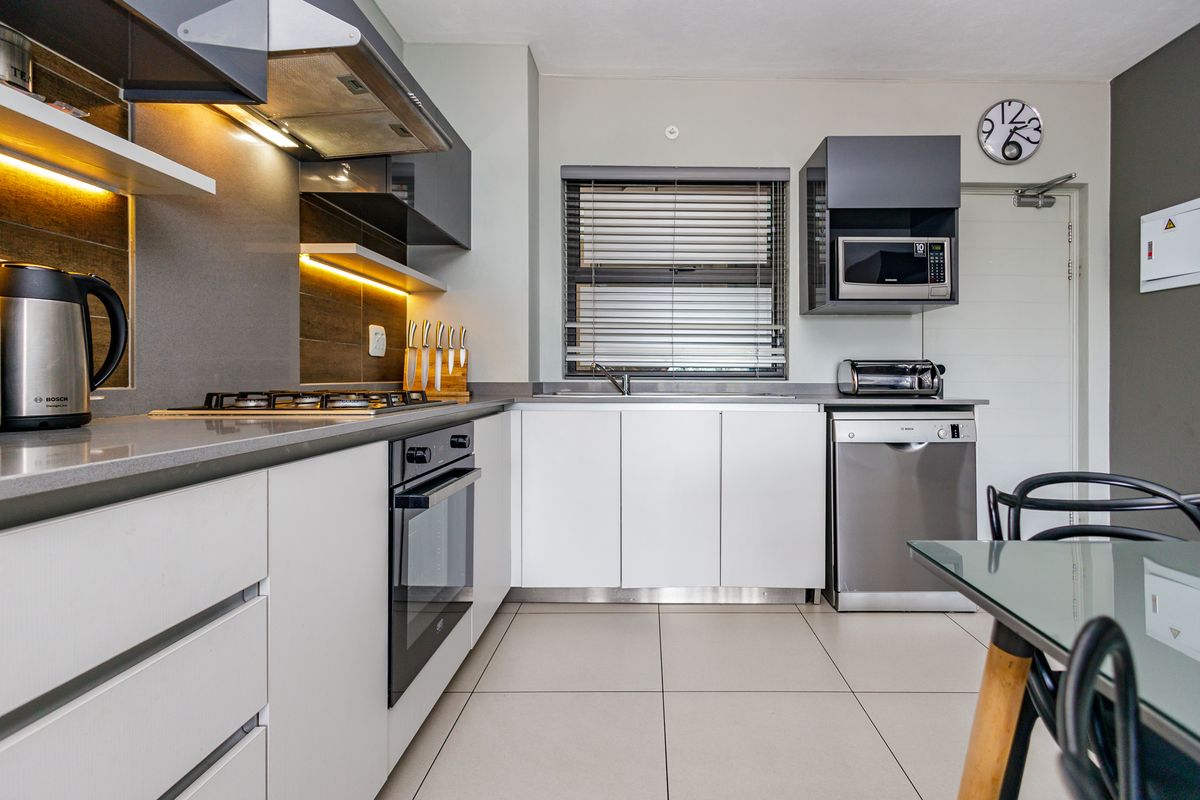 Modern kitchen featuring sleek white cabinetry, grey stone countertops, integrated oven, gas hob, extractor fan, and built-in microwave with tiled flooring.