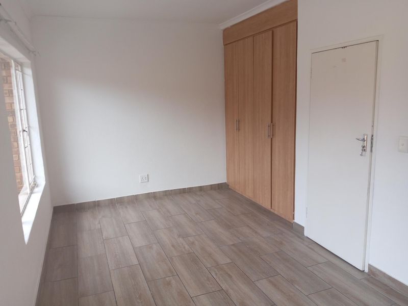 A bright, empty bedroom featuring wood-look tiled flooring and built-in wooden cupboards.