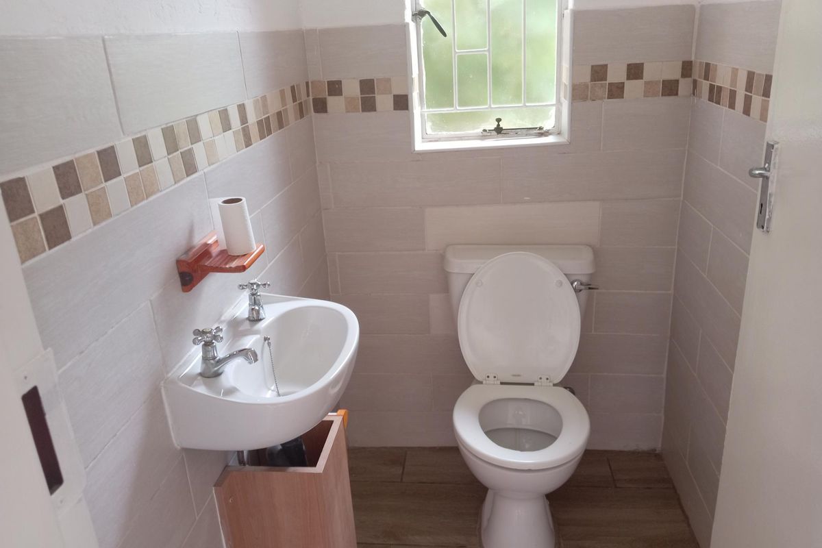 A compact guest bathroom featuring a wall-mounted basin, a standard toilet, and neutral wall tiling with a decorative mosaic border.