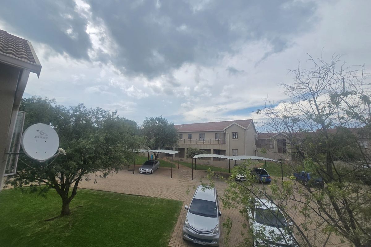 View of the apartment complex grounds featuring paved parking areas, covered carports, and landscaped garden space.