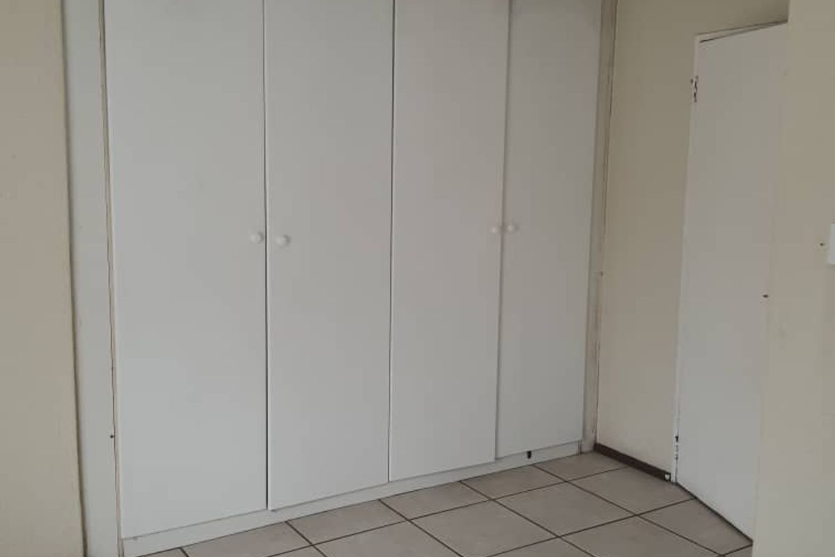 A bedroom featuring built-in cupboards with white doors and tiled flooring, showing signs of wear and requiring cosmetic updates.