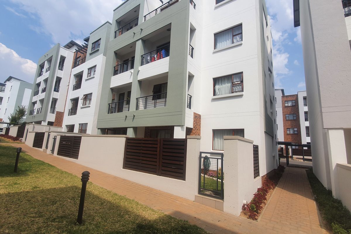 Exterior view of a modern multi-story apartment complex featuring balconies, paved walkways, and landscaped garden areas.