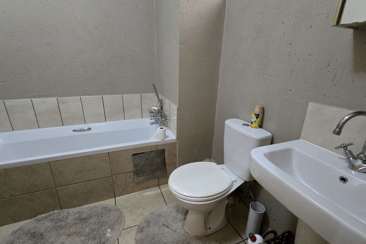 A functional bathroom featuring a bathtub, pedestal basin, and toilet with neutral wall finishes and tiled flooring.