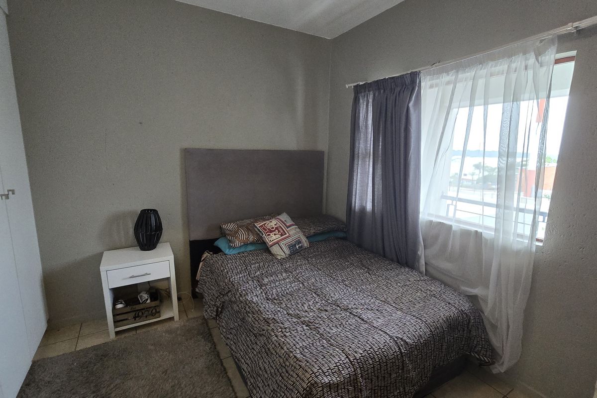 A functional bedroom featuring tiled flooring, a built-in wardrobe, and natural light provided by a window with curtain tracks.
